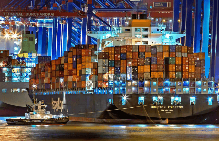 Buque portacontenedores amarrado en un puerto de noche, con un remolcador a su lado