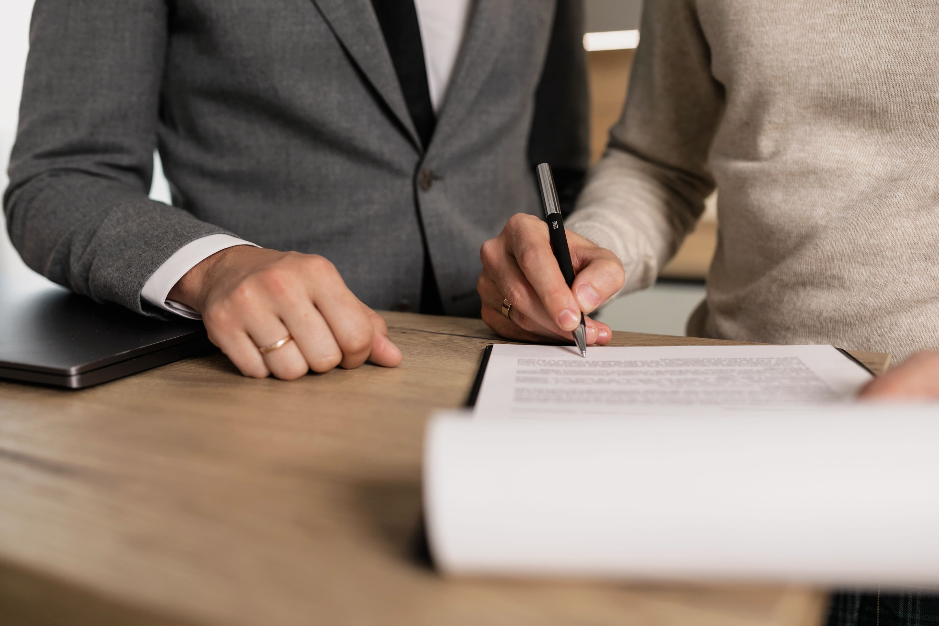 Dos personas revisando y firmando un documento sobre una mesa de madera
